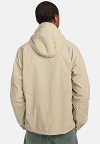 Beige hættejakke med en afslappet pasform, lavet af let vævet materiale, med et enkelt design og uden synlige mønstre eller hardware.