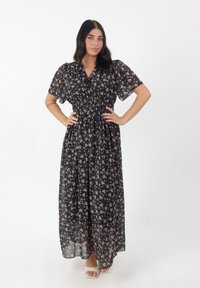 Maxi-jurk van doorschijnende zwarte stof met een klein roze bloemenpatroon. Kenmerkt zich door korte pofmouwen en een elastische taille voor een vloeiende uitstraling.