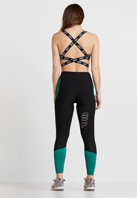 Czarne legginsy sportowe z zielonymi akcentami i siateczkową fakturą, połączone z czarnym sportowym stanikiem w krzyż, z markowymi ramiączkami.