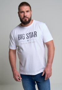 Camiseta de algodón blanca con mangas cortas que presenta un audaz estampado gráfico en negro con el texto "BIG STAR" y "Tu Vida. Tus Jeans." en gris debajo.