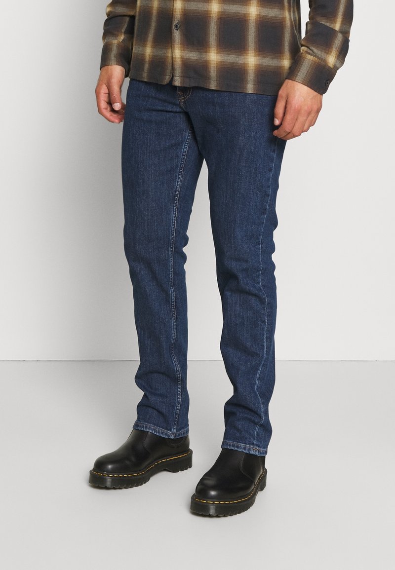 Vaqueros de mezclilla azul oscuro con un diseño de ajuste slim, detallados con costuras naranjas, combinados con botines Chelsea negros con suela texturizada.