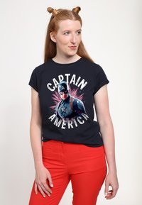 Marineblå t-shirt med grafik af en superhelt og teksten "CAPTAIN AMERICA," parret med livlige røde bukser.