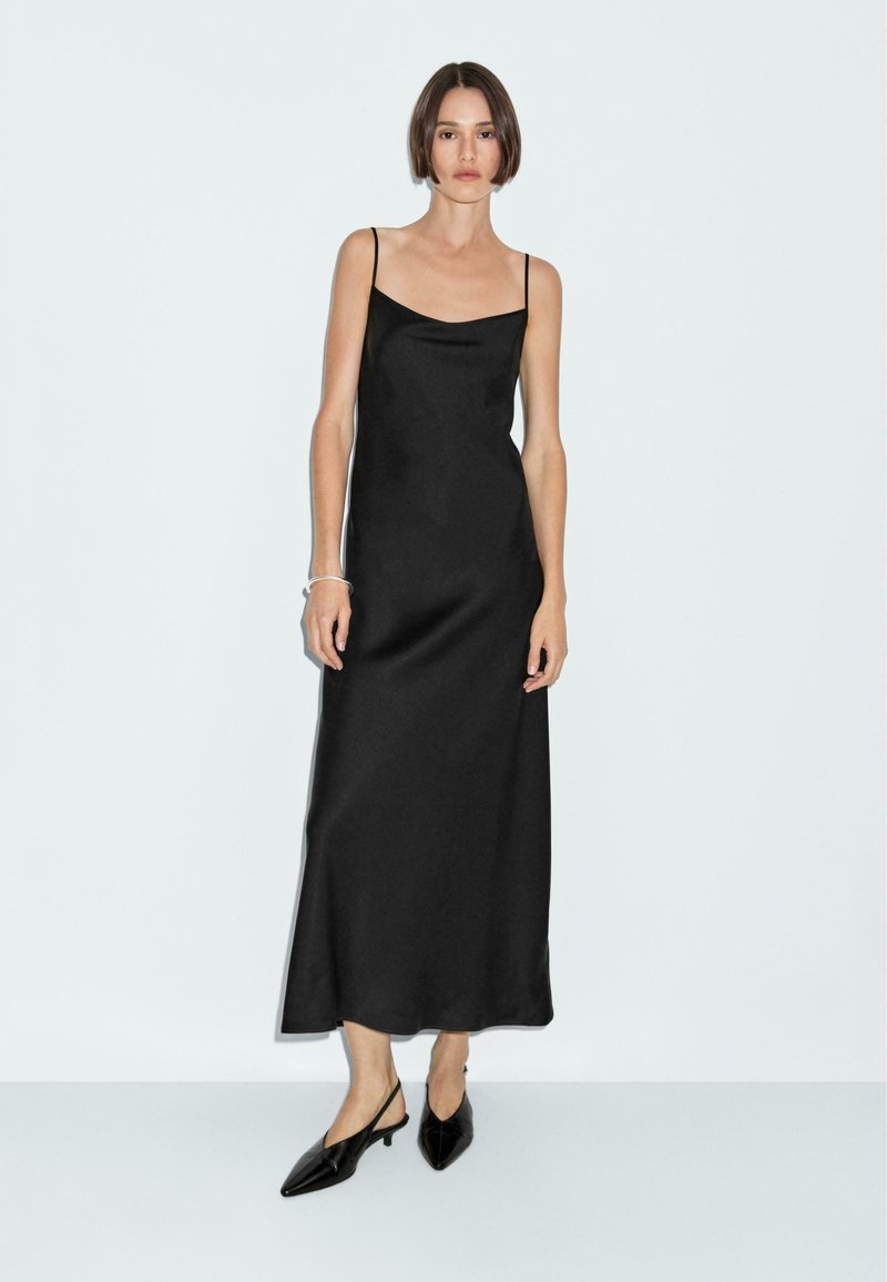 Zwarte satijnen maxi-jurk met dunne bandjes, met een gladde textuur en een vloeiende silhouet. Gecombineerd met zwarte spitse slingback-schoenen.