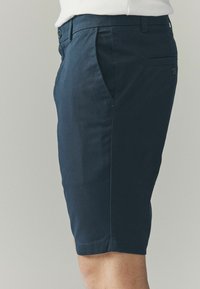 Mørkeblå shorts lavet af letvægtigt stof, med flad frontdesign, sidelommer og en enkelt baglomme med knaplukning.