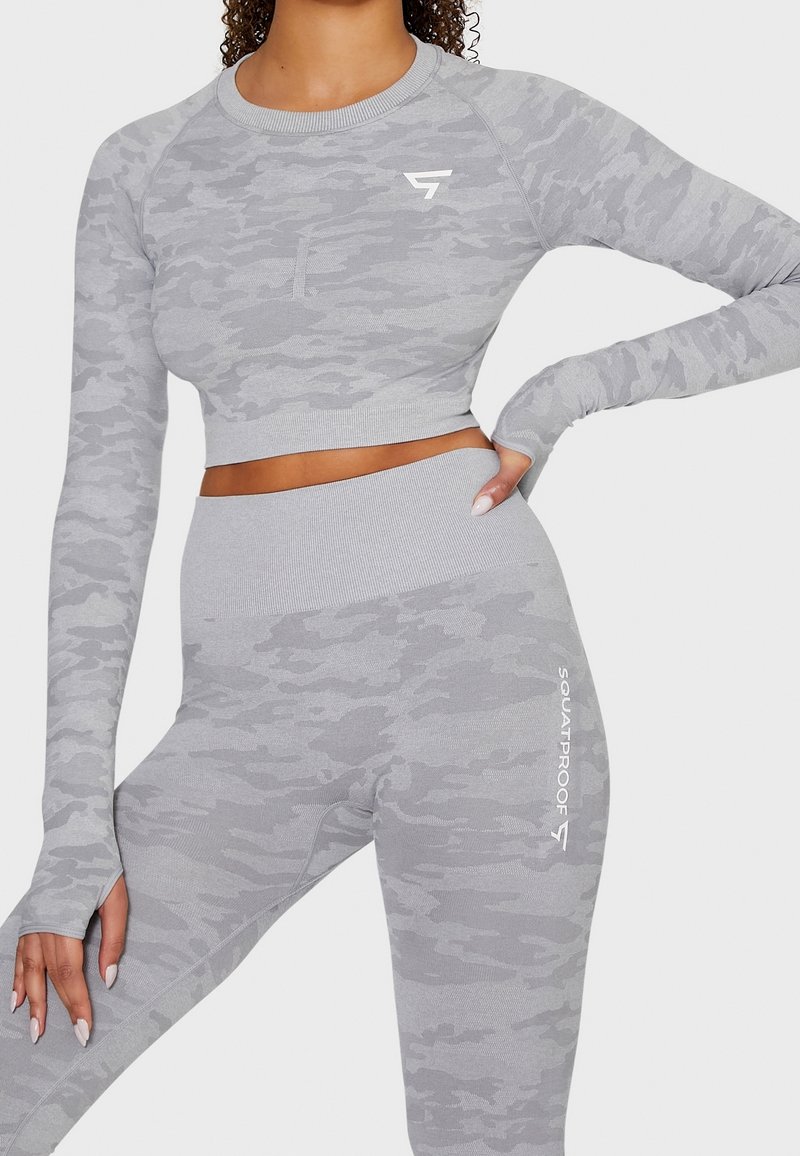 Graues Camouflage-Sportset bestehend aus einem kurzen Langarmoberteil und hochgeschnittenen Leggings. Das Material ist dehnbar und gerippt; das Logo ist in Weiß gedruckt.