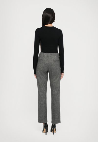 Schwarzes Langarmoberteil kombiniert mit grauen karrierten Hosen, die einen geraden Schnitt und einen strukturierten Stoff aufweisen. Das Outfit wird mit schwarzen High Heels abgerundet.