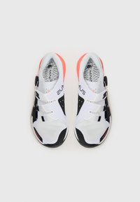 Scarpe da ginnastica bianche e nere con un design in rete, dotate di tre cinturini in Velcro, una suola testurizzata e dettagli corallo sul tallone.