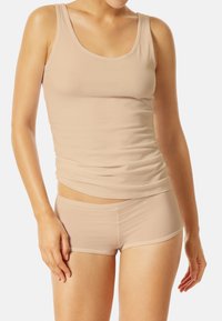 Un top débardeur beige et un shorty assorti en tissu extensible et lisse. Le débardeur a un col rond et un design ajusté, mettant en valeur la silhouette.