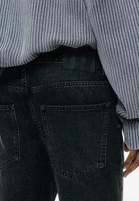 Jeans neri in denim con una vita testurizzata e tasche posteriori. Abbinati a un top grigio a maniche lunghe con costine. Design minimalista.