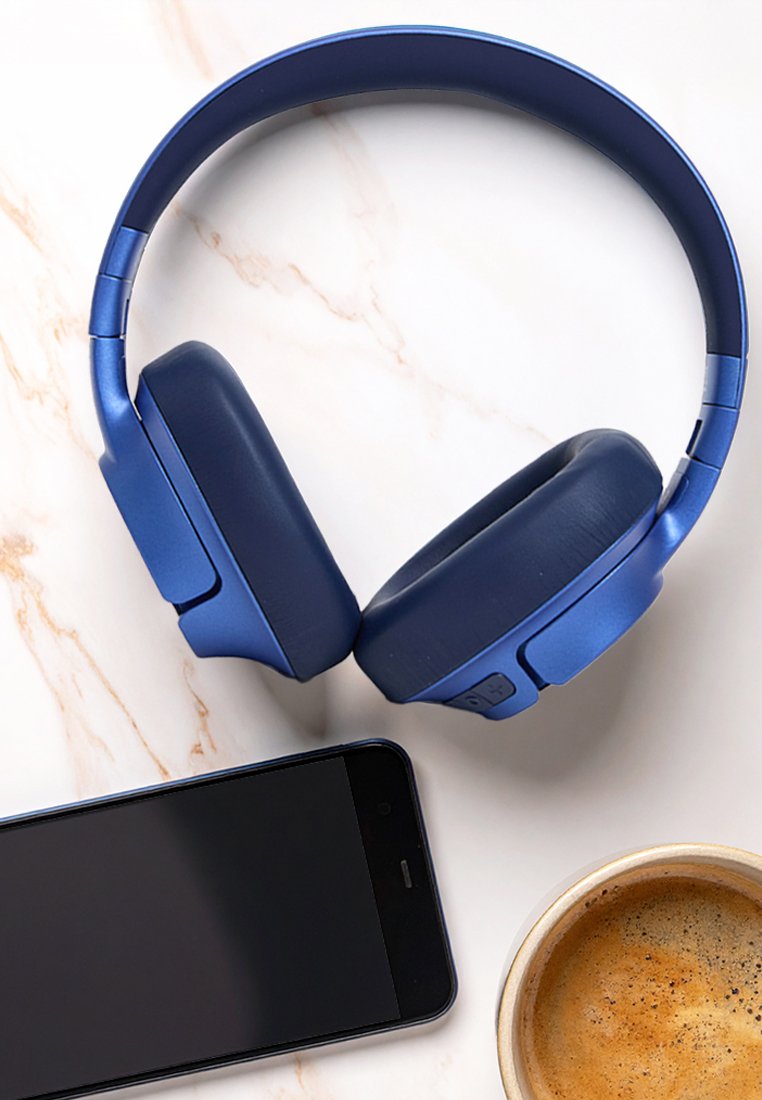 Blaue drahtlose Kopfhörer, schwarzes Smartphone und eine Tasse Kaffee auf einer weißen Marmoroberfläche, die ein lässiges Tech- und Entspannungs-Setup suggerieren.