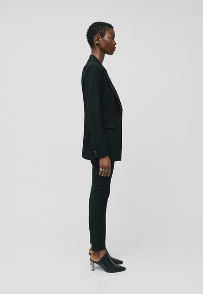 Black tailored blazer with notched lapels, slim black trousers, and black mules with a metallic heel. Smooth fabric with structured fit.