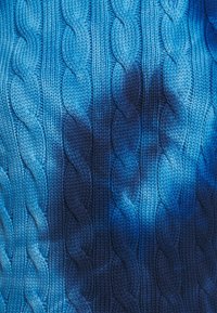Tissu bleu tricoté avec un motif répétitif de mailles torsadées verticales et des ombres accentuant la profondeur de la texture.