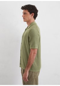 Short-sleeve polo shirt in textured light green fabric, featuring a collar, button front, and a relaxed fit.