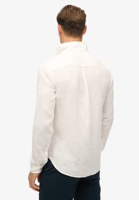 Camisa de lino beige claro con yugo trasero, mangas largas y dobladillo redondeado. Presenta puños con botones y un diseño de cuello casual.