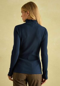 Námornícky pruhovaný rolák so volánovým golierom a dlhými rukávmi. Detail s gombíkmi na manžetách. Nosené s pruhovanými hnedými nohavicami.