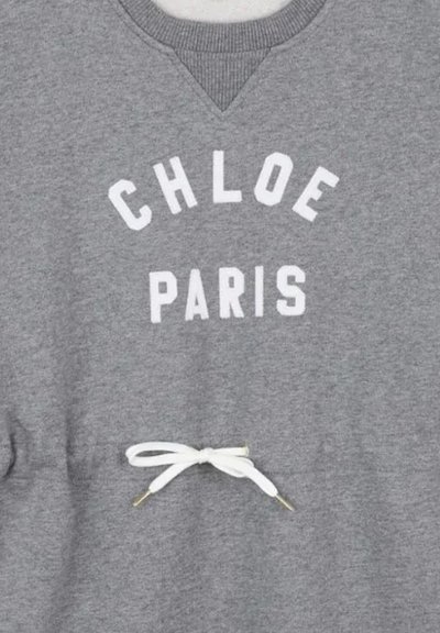 Szara bluza z białym napisem "CHLOE PARIS" oraz białym sznurkiem związanym w kokardę poniżej napisu w okolicy talii.