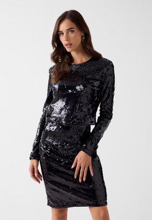 Vestido negro con lentejuelas, de manga larga, ajustado al cuerpo, con cuello redondo y superficie texturizada que refleja la luz para un interés visual adicional.