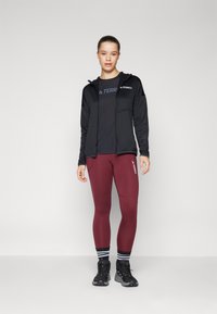 Must have mustad sviiter musta t-särgi peal, koos marooni värvi legginside, mustade matkasaabaste ja must-valgete triibuliste sokkidega.