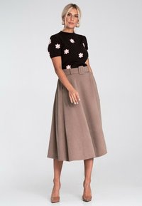 Czarny sweter z krótkim rękawem z różowymi aplikacjami w kształcie kwiatów, zestawiony z beżową spódnicą w kształcie litery A o wysokim stanie i plisowaniach oraz cielistymi szpilkami, gładka tekstura.