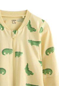 Ljusgul zip-up-jacka med tecknade gröna krokodiler i olika uttryck och mönster. Mjuk tyg, avslappnad design.