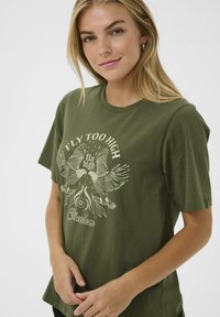 T-shirt en coton vert olive avec un col rond et des manches courtes, présentant un imprimé graphique blanc de oiseaux et un texte stylisé.