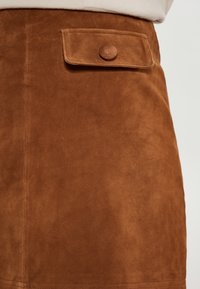 Bruine suède rok met een voorzak met knoopsluiting, een gladde textuur en een eenvoudig ontwerp.