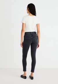 Black skinny jeans with a high waist, back pockets, and a smooth fabric texture paired with a short-sleeve white t-shirt and studded flats.