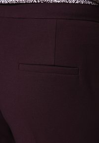 Mörkröda byxor med en subtil textur och en enda bakficka. Overdelen har ett mönstrat kantband vid midjan.