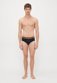 Schwarze Badebrief mit oranger Logo-Bande. Glatte Textur und figurschmeichelndes Design mit niedriger Taille. Keine zusätzlichen Muster oder Details.