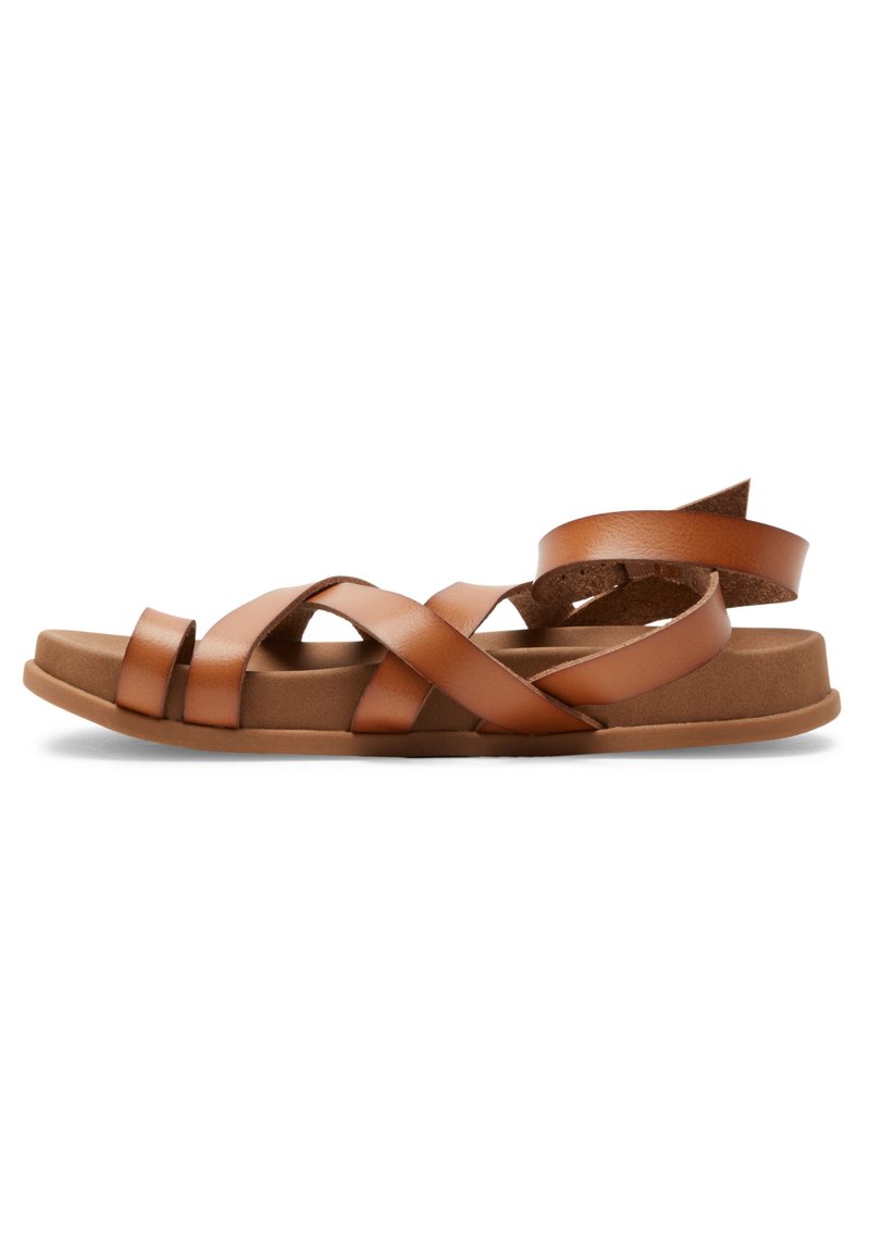 Sandales en cuir marron avec des brides croisées, semelles plates et talon légèrement surélevé. Texture douce et design minimaliste.