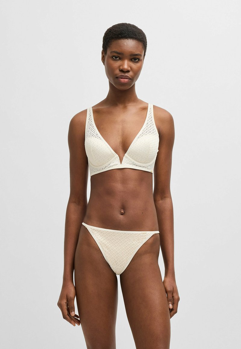 Light cream bra and thong set made of textured fabric with a geometric pattern. The bra features a deep V-neck and wide straps.