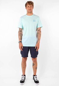 T-shirt bleu clair en dégradé avec des manches courtes et un petit motif imprimé sur la poitrine, associé à des shorts navy et des baskets montantes noires.