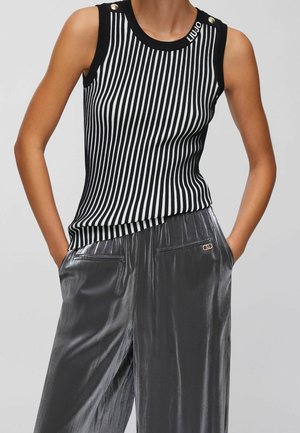 Haut sans manches à rayures verticales noires et blanches avec détails de boutons sur les épaules, associé à un pantalon ample, brillant, gris foncé avec poches.