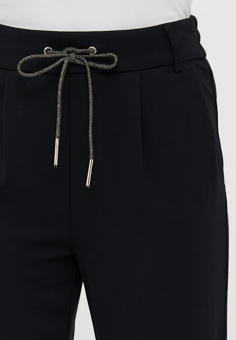 Schwarze Hosen mit einem Kordelzugbund und metallischen Akzenten, Falten vorne und einem glatten, strukturierten Stoff.