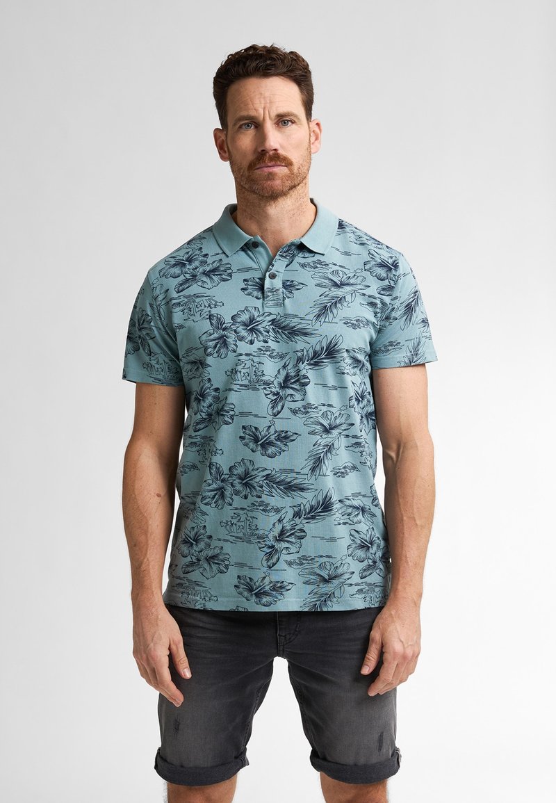 Pánské polo tričko v barvě teal s tmavým květinovým a listovým potiskem, s krátkým rukávem a límečkem. V kombinaci s tmavými šortky s ohrnutým lemem.