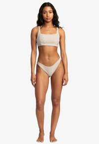 Ensemble de bikini rayé comprenant un haut bandeau avec de larges bretelles et un bas taille basse ; couleurs incluent des rayures beige et crème ; texture de tissu lisse.