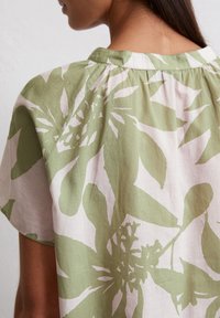 Blouse florale verte et rose, fabriquée en tissu léger. Présente un col froncé et des manches courtes avec une coupe décontractée.