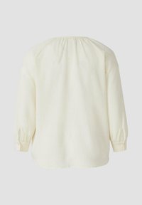 Cremefarbene, strukturierte Bluse mit langen Ärmeln und gerafften Details an Schultern und Ärmelbündchen. Gerade Saumlinie am unteren Ende.