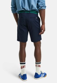 Marineblå shorts med en grønnstripet midjebånd, med baklommer og en skreddersydd passform, kombinert med blå sneakers og hvite, mønstrede sokker.