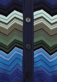Cardigan tricotat cu un model în zigzag, având nuanțe de albastru, verde, negru și bej. Închidere frontală cu nasturi și placket rib confortabil de culoare bleumarin.