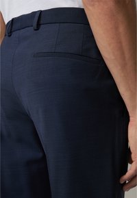 Marineblauwe op maat gemaakte broek met een soepele textuur, voorzien van een achterzak en een tailleband met lussen voor een riem.