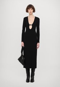 Melna ribota kleita ar dziļu V veida kakla izgriezumu un sudraba akcentu. Modelis tur melnu somu, uzvilcis melnus augstus zābakus. Vienkāršs, elegants dizains.
