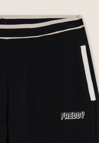 Pantalones deportivos negros con una cinturilla blanca a contraste con rayas, un bolsillo lateral y el logo "FREDDY" en letras blancas.