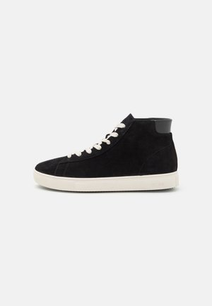 Czarny zamszowy sneaker za kostkę z białymi sznurowadłami i białą gumową podeszwą, pokazany z boku na jednolitym tle.
