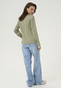 Grön långärmad topp med vita randiga manschetter, kombinerad med ljusblå vida jeans. Enkelt mönster, mjuk textur och avslappnad passform.