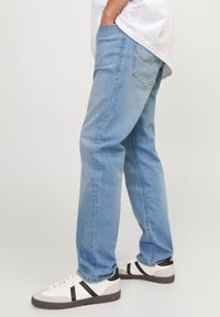 Lyseblå denimjeans med rette ben, subtile sømdetaljer og avslappet passform, kombinert med hvite og svarte joggesko.