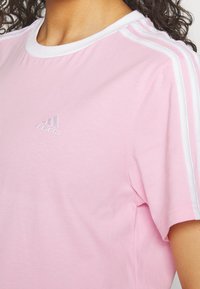 Rosa bomull t-shirt med vitt trim och tre vita ränder på ärmarna. Har en liten broderad Adidas-logotyp på bröstet.