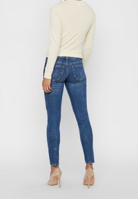 Smal blåjeans med midjehöjd, detaljerad sömnad och bakfickor. Kompletterad med en krämfärgad långärmad topp och beige klackar.