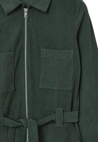 Salopette en velours côtelé verte avec une fermeture éclair sur le devant, deux poches plaquées et une ceinture assortie. Présente une texture à côtes verticales.