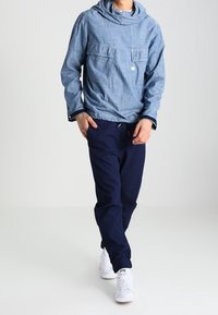 Casuale blauwe hoodie met twee voorzakken, gecombineerd met marineblauwe broek en witte sneakers, met een ontspannen pasvorm en een gladde textuur.